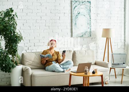 Eine kahlköpfige Frau sitzt bequem auf einer Couch und taucht in ein Buch ein, während sie Musik hört. Stockfoto