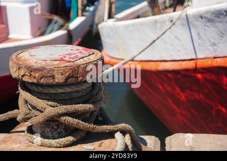 Verrosteter Schiffspoller mit Seilen, die Boote am Hafen an einem sonnigen Tag sichern Stockfoto