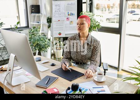 Eine kahlköpfige Frau mit auffälligen rosa Haaren konzentriert sich auf ihre Aufgaben, während sie an einem modernen Schreibtisch sitzt. Stockfoto