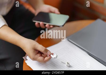 Frau nimmt kabellose bluetooth-Kopfhörer heraus. Kopfhörer mit Smartphone Stockfoto