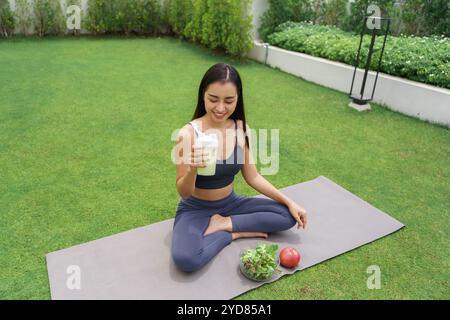 Sportliche asiatische Frau in Sportbekleidung trinkt Proteinshake aus der Flasche nach dem Training für Energie Vitalität im Morning Park Sportswom Stockfoto