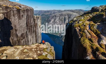 Zwei Personen stehen am Rande der Kjeragbolten-Klippe in Norwegen und blicken auf einen atemberaubenden Blick auf den Fjord und die umliegenden Berge. Co Stockfoto