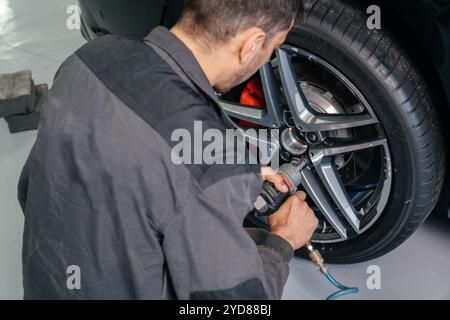 Mechaniker ändern Autorad in der Auto-Werkstatt mit einem elektrischen Bohrer, um die Schrauben zu lösen.Konzept der Service oder Austausch. Stockfoto