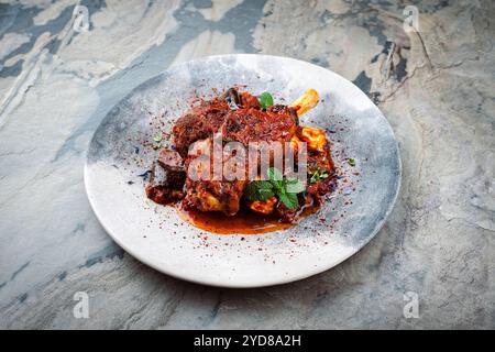 Traditionelle geschmorte, langsam gekochte Lammknöchel mit Auberginen und griechischem Fetakäse serviert als Nahaufnahme in einem nordischen Design-Teller mit Stockfoto