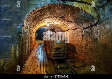 Rostiger Bergbauzug in einem dunklen Tunnel unter dem Berg mit Gleisen und Holzboden, Goldmine Stockfoto