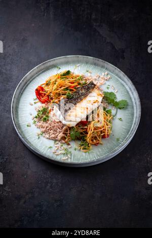 Gebratenes Kabeljaufilet mit Papaya-Som-tam-Salat und rotem Reis als Nahaufnahme auf nordischem Design-Teller mit Kopierraum Stockfoto