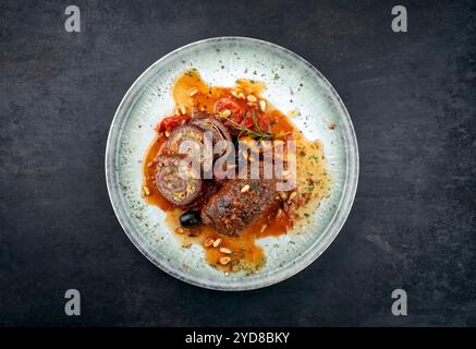 Traditionelle langsam gekochte deutsche Wagyu-Rindfleischrouladen mit Oliven und Pinienkernen serviert in scharfer Rotweinsauce als Blick von oben in einem NOR Stockfoto