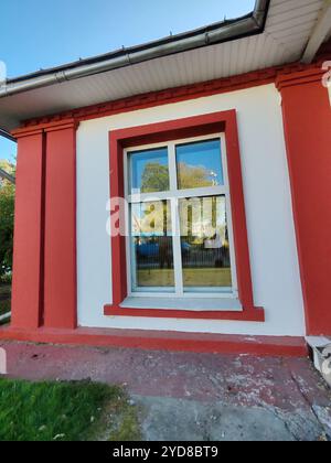 Ein Gebäude mit einem rot umrandeten Fenster in einer weißen Wand, das die Umgebung im Freien reflektiert. Dieses Foto unterstreicht den ästhetischen Reiz von Stockfoto