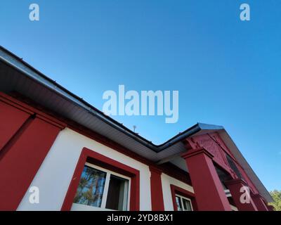 Ein Gebäude mit einem rot umrandeten Fenster in einer weißen Wand, das die Umgebung im Freien reflektiert. Dieses Foto unterstreicht den ästhetischen Reiz von Stockfoto