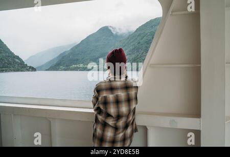 Frau genießt Fjordlandschaften auf der norwegischen Fähre mit nebelgrünen Bergen im Hintergrund. Die Szene fängt das Wesen entspannter Reisen und Erkundungen ein Stockfoto