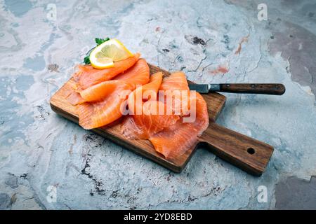 Traditioneller norwegischer Räucherlachs in Scheiben mit Petersilie und Zitrone serviert als Nahaufnahme auf rustikalem hölzernem Schneidebrett mit Textfeld Stockfoto