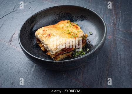 Traditionelles griechisches Moussaka mit Hackfleisch, Auberginen und Bechamelsauce, serviert als Nahaufnahme in einer Schüssel im nordischen Design auf einem Steinbrett Stockfoto