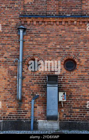 Ziegelwand einer Fabrik mit runden Fenstern und Lüftungsrohren Stockfoto