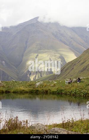 Ein friedlicher Moment, in dem zwei Personen an einem kleinen, ruhigen Teich sitzen und die ruhige Berglandschaft um sie herum genießen. Stockfoto