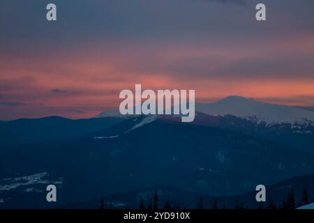 Ein feuriger Sonnenuntergang zeigt den Himmel über einer majestätischen Bergkette. Silhouettenspitzen stehen hoch vor einem atemberaubenden Himmel in der Dämmerung. Stockfoto