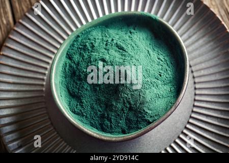 Grünes Spirulina-Pulver in einer schwarzen Schüssel auf einem Tisch Stockfoto