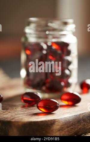 Rote Krillölpillen oder Kugeln auf einem Holztisch und in einem Glasgefäß Stockfoto