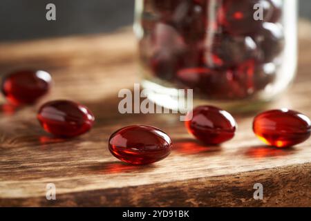 Rote Krillölpillen oder Kugeln auf einem Holztisch, Nahaufnahme. Gesundes Nahrungsergänzungsmittel reich an Omega-3. Stockfoto