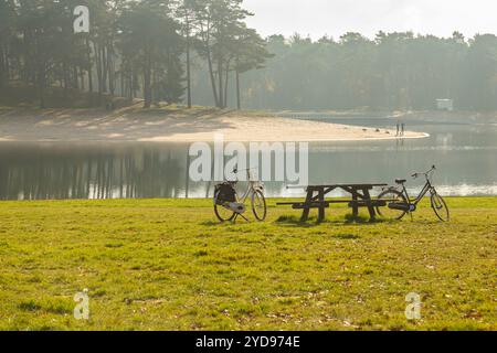 Rastplatz am See im Wald mit zwei Fahrrädern am Ufer und ein Paar am Strand im Hintergrund am frühen Herbstmorgen Stockfoto