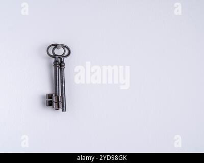 Zwei rostige eiserne Schlüssel hängen an einem Nagel an einer weißen Wand. Stockfoto