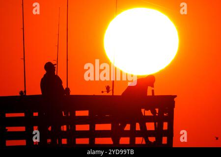 Isle Of Palms, Usa. Oktober 2024. Sportfischer, die vom Sonnenaufgang umrahmt werden, werfen ihre Linien, während die riesige orangene Sonne über dem Atlantischen Ozean vom Isle of Palms Pier am Front Beach am 25. Oktober 2024 in Isle of Palms, South Carolina, aufgeht. Sonniges und warmes Wetter wird für die nächsten Wochen vorhergesagt. Quelle: Richard Ellis/Richard Ellis/Alamy Live News Stockfoto