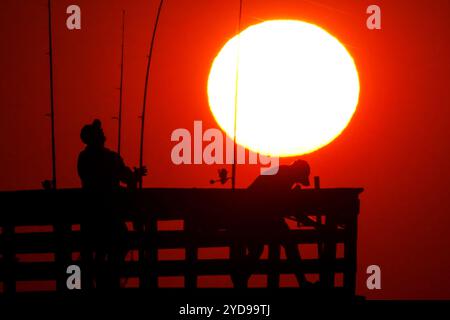 Isle Of Palms, Usa. Oktober 2024. Sportfischer, die vom Sonnenaufgang umrahmt werden, werfen ihre Linien, während die riesige orangene Sonne über dem Atlantischen Ozean vom Isle of Palms Pier am Front Beach am 25. Oktober 2024 in Isle of Palms, South Carolina, aufgeht. Sonniges und warmes Wetter wird für die nächsten Wochen vorhergesagt. Quelle: Richard Ellis/Richard Ellis/Alamy Live News Stockfoto