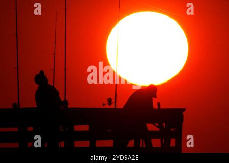 Isle Of Palms, Usa. Oktober 2024. Sportfischer, die vom Sonnenaufgang umrahmt werden, werfen ihre Linien, während die riesige orangene Sonne über dem Atlantischen Ozean vom Isle of Palms Pier am Front Beach am 25. Oktober 2024 in Isle of Palms, South Carolina, aufgeht. Sonniges und warmes Wetter wird für die nächsten Wochen vorhergesagt. Quelle: Richard Ellis/Richard Ellis/Alamy Live News Stockfoto