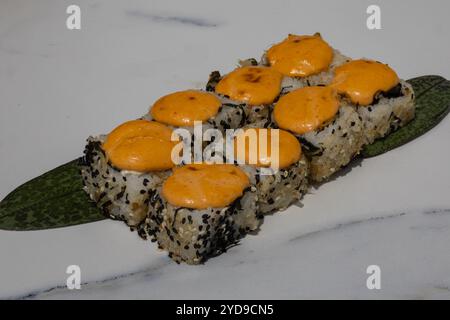 Nahaufnahme von Sushi-Brötchen mit würzigem Mayo-Belag auf grünem Blatt, serviert auf weißem Teller. Japanische Küche, traditionelle Küche und Gourmetrestaurant Stockfoto