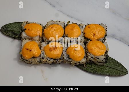 Scharfe Sushi-Brötchen mit cremigem Topping, serviert auf grünem Blatt und weißem Teller unter natürlichem Licht Stockfoto