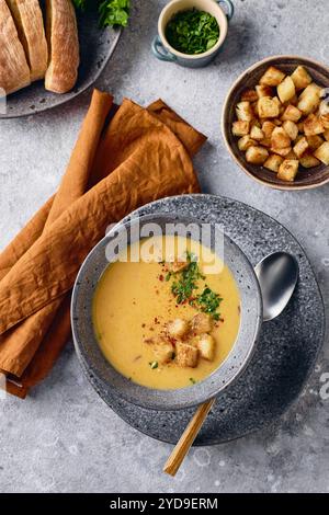 Schüssel Kartoffelpüree mit einem Löffel auf dem Teller. Die Schüssel wird mit gelbem Suppenpüree gefüllt und mit Croutons und Parseln belegt Stockfoto