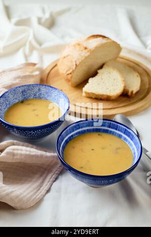 Zwei Schüsseln cremige Kartoffelsuppe, Löffel, Serviette und hölzerne Schneidebrett mit einem Laib Brot und geschnittenen Stücken. Stockfoto