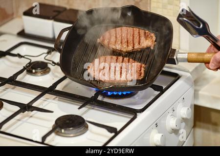 Der Prozess, zwei Rindersteaks in der Pfanne zu kochen, die Hände des männlichen Küchenchefs salzen rohes Fleisch, Nahaufnahme Stockfoto