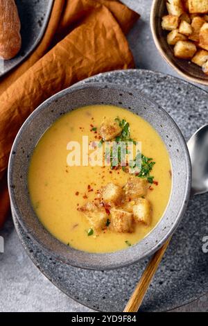 Schüssel Kartoffelpüree mit einem Löffel auf dem Teller. Die Schüssel wird mit gelbem Suppenpüree gefüllt und mit Croutons und Parseln belegt Stockfoto