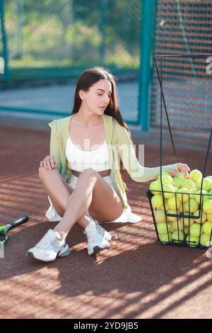 Schöne Frau, die Tennisball aus dem Korb auf dem Platz nimmt Stockfoto