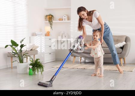 Die lächelnde junge Frau und ihre Tochter putzen zu Hause den Boden mit schnurlosem Staubsauger Stockfoto