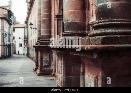 Nahaufnahme der verwitterten Steinsäulen an einer historischen Gebäudefassade mit detaillierter Textur und architektonischen Elementen. Eine ruhige, enge Straße Stockfoto