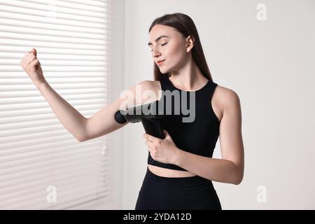 Frau, die das Schlaggerät benutzt, um den Bizeps drinnen zu entspannen Stockfoto