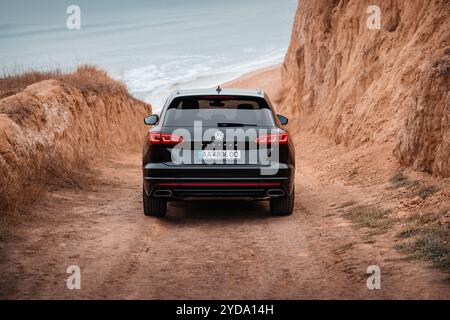 Volkswagen Touareg fährt einen Hügel hinunter zum Strand. Schwarzer VW-SUV auf einer Feldstraße in der Nähe von lehmfarbenen Klippen am Meer. Stockfoto