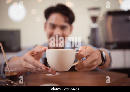 Dieser junge Barista, der einen Latte Kaffee zubereiten möchte, um die Gäste sowohl in Aussehen als auch im Geschmack zufriedenzustellen, ist diese Tasse Kaffee Stockfoto