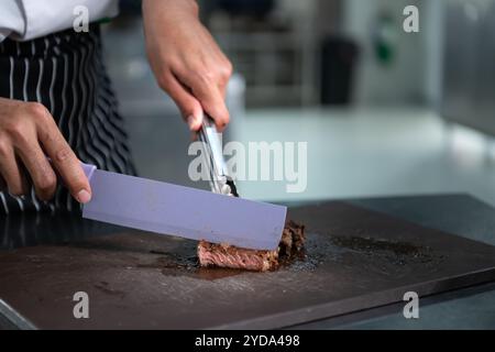 Junger Koch schneidet mittelseltenes Steak, nachdem es fertig gegrillt wurde. Stockfoto