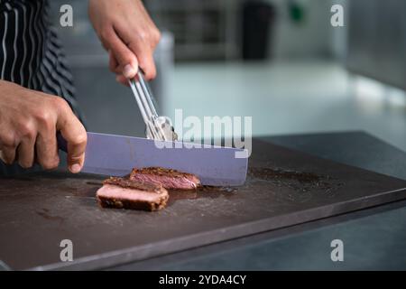 Junger Koch schneidet mittelseltenes Steak, nachdem es fertig gegrillt wurde. Stockfoto