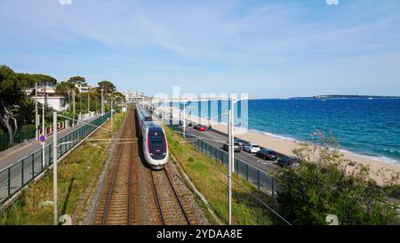 Ein TGV-Hochgeschwindigkeitszug, der entlang der malerischen Mittelmeerküste in Frankreich gleitet. Die Bahnstrecke verläuft parallel zum glitzernden blauen Meer. Stockfoto