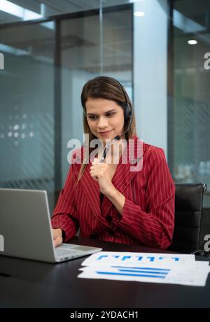 Junge Frau, die in einem Callcenter arbeitet, das als Berater für verschiedene Informationen über Kunden fungiert, die anrufen, um sich zu erkundigen oder um eine zu bitten Stockfoto
