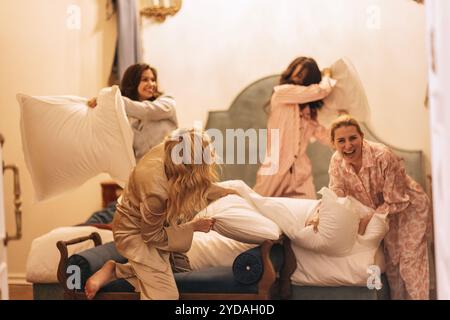 Junge Frauen verschiedener Rassen im Pyjama, die sich auf einem Bett in einem Hotel amüsieren Stockfoto