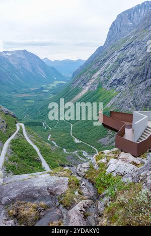 Eine Person steht auf einem Bahnsteig mit Blick auf eine gewundene Straße und ein Tal in Norwegen. Die Straße schlängelt sich den steilen Berghang hinunter und führt zu einem Grün Stockfoto