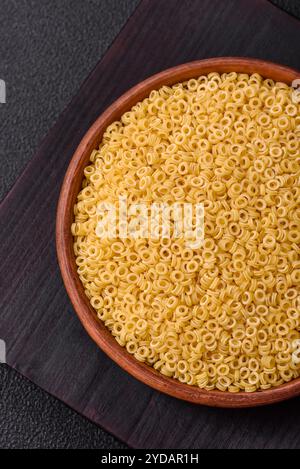 Rohe Aellini-Nudeln aus Hartweizen mit Salz und Gewürzen auf dunklem Betonhintergrund Stockfoto