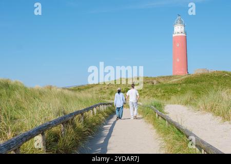 Zwei Personen schlendern auf einem gewundenen Pfad neben einem historischen Leuchtturm auf der malerischen Insel Texel, Niederlande Stockfoto