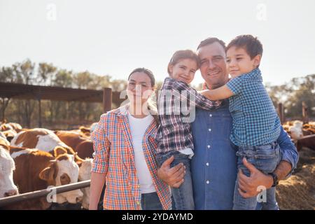 Eine junge glückliche Familie von Bauern in einem Kuhstall. Eine lächelnde Frau, ein Mann und zwei Kinder in lässiger Kleidung kümmern sich um die Haustiere auf dem Stockfoto