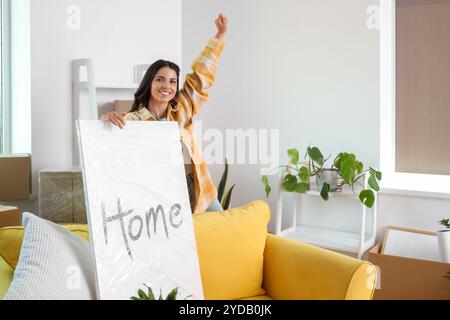 Glückliche junge Frau mit eingewickeltem Poster im Zimmer am Umzugstag Stockfoto