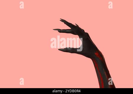 Schwarze Hexenhand mit Krallen auf rosa Hintergrund. Halloween-Feier Stockfoto
